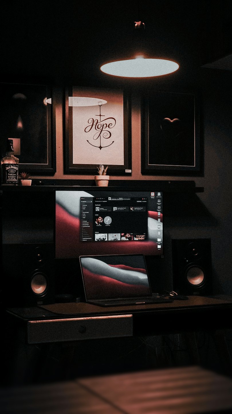 Computer setup with monitors, laptop, and artwork on shelf.